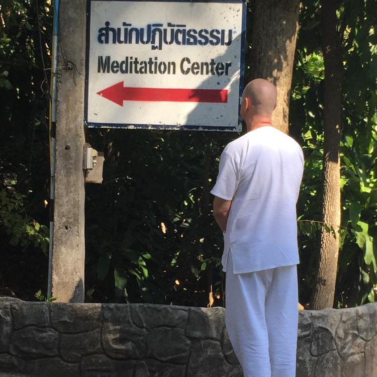 Teacher David Roylance standing near a meditation center sign in Thailand